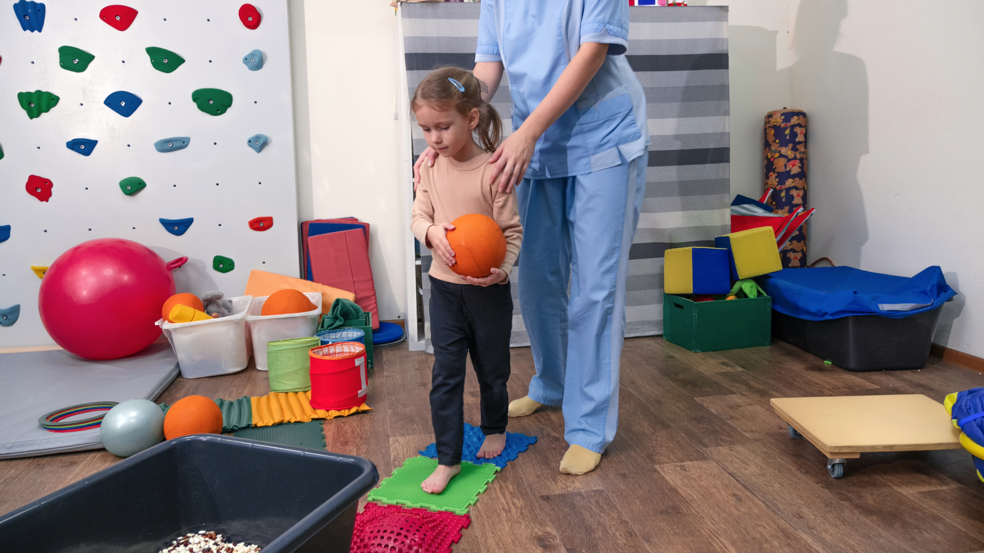 Menina com bola laranja a brincar com uma terapeuta ocupacional